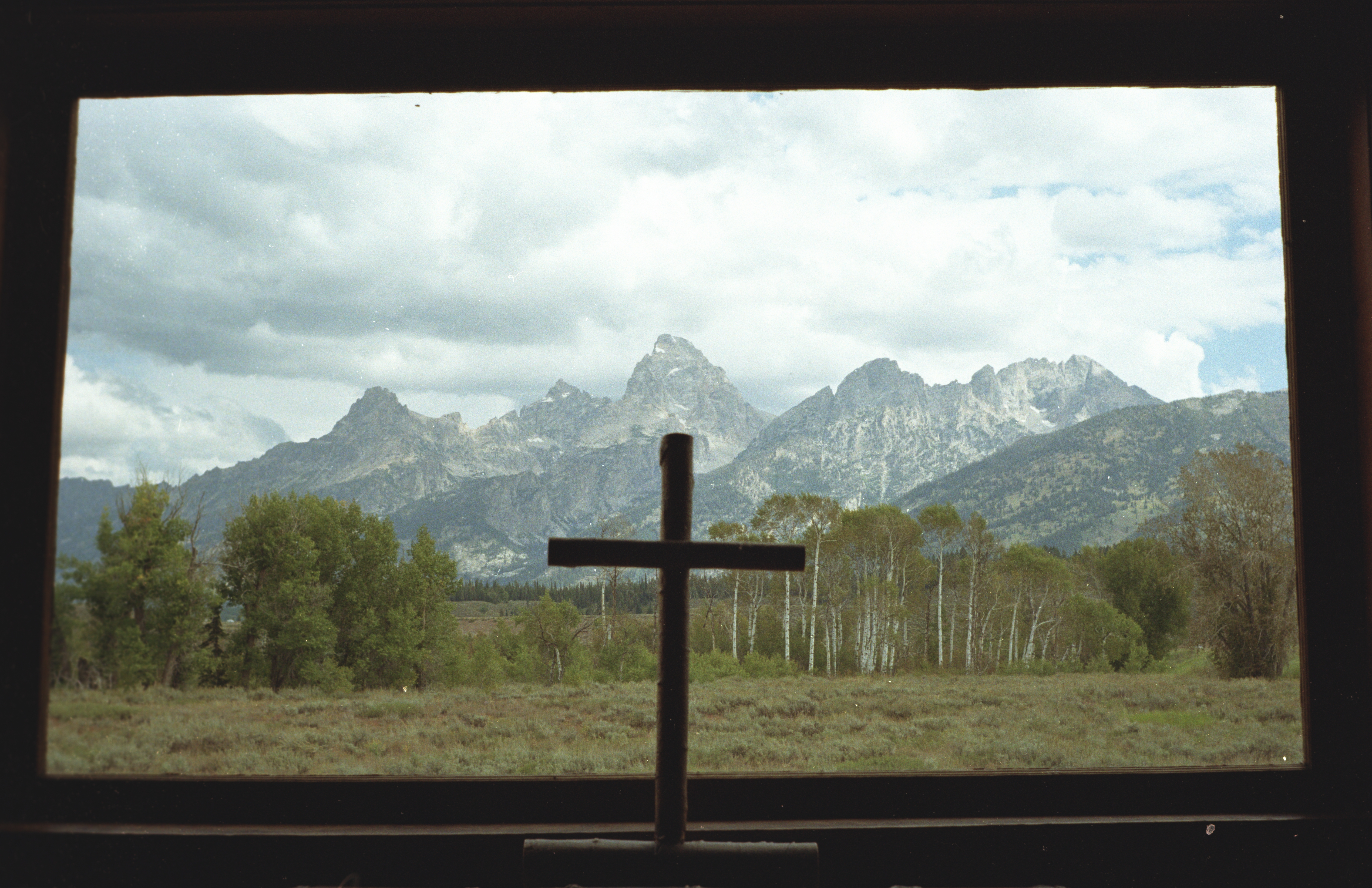 Picture of a cross looking out a window on mountains